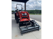 Red tractor with a front attachment on a concrete surface with trees and sky in the background